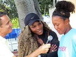 A reporter holding a microphone to Osaka with Williams to the side smiling
