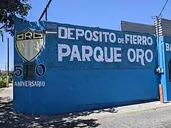 An exterior wall, painted blue, with text commemorating the former stadium.