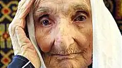 Photograph of an elderly, pale-skinned woman with a white headcovering.