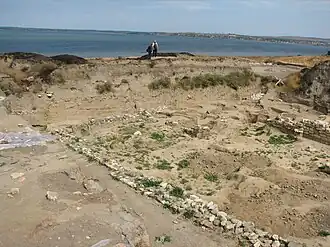 The remains of the wall of a small structure are seen in the foreground, the Sea of Azov is visible in the background.