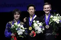 A photograph of Shoma Uno, Nathan Chen and Mikhail Kolyada (from left to right) with medals around their necks and flowers in their hands.