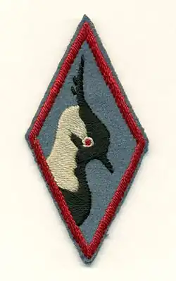 A diamond shaped patch on blue felt with heavy red trim. The central image is a black and white profile of a peewit bird (Lapwing) highlighted with a red eye.