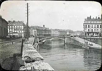 Loading around 1900 of a boat moored at the foot of the Place de la Petite-Hollande&nbsp;[fr] near the Hôtel de La Villestreux&nbsp;[fr]. The Palais de la Bourse is on the opposite bank. The Place du Commerce and Île Feydeau&nbsp;[fr] are connected by the Pont de la Bourse.