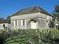 A small, rectangular building next to some gravestones.