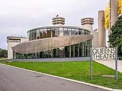 The Queens Theatre, occupying the former Theaterama. The glass structure in the foreground contains the Queens Theatre's entrance, which was added in 2009. Behind the structure is the original Theaterama, a concrete building.