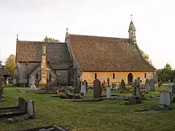 A church seen from the north with an extensive roof. On the right is the nave with a bellcote at the west end; on the left is the chancel with the vestry.