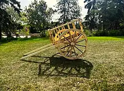 A handcrafted, wooden, Red River cart, made entirely of wood using mortise and tenon, sitting in a field framed by trees.