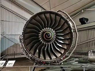 Rolls-Royce Trent 900 116 inch diameter fan. The fan has supersonic relative velocities in the outer half which result in shock waves in the passages. Visually evident are the blade leading edge sweep which changes from hub to tip from forward to backward to forward and the blade twist which varies from almost axial at the hub to almost circumferential at the tip. The shape of the blade positions the shock far enough behind the leading edge to prevent expulsion of the shockwave beyond the tip leading edge (prevents surge and flutter). Each radial section with its contribution to leading edge sweep and blade twist has its centrifugal force acting close to a radial line which minimizes stress due to rotation.[82][83]
