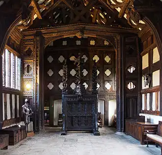 Indoor photograph of large Tudor hall with large, elaborately carved screen at one end
