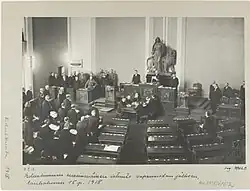 Parliament is convening for the first time after the war. White and German soldiers dominate the picture while only one person from the opposition social democrats is present. Thus, it was sarcastically called a Rump Parliament.