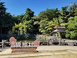 The Ryukyu Mura sign in the center of the village area, featuring the park's mascots.