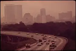 Cars travel over a highway overpass with the smog-obscured Birmingham skyline in the background