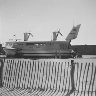 Passenger hovercraft resting on beach adjacent to swimming complex seawall in background behind a safety cordon made from paling fence