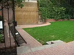 A grass field with brick pathway lining the side of it. A waterfall and green wall is visible in the background