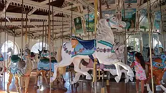 A white carousel horse with a blue saddle and bridle on a white historic carousel