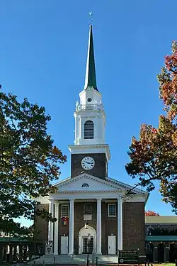 The front façade of a nineteenth-century brick church building with columns and Greek Revival pediment, cupola, and steeple