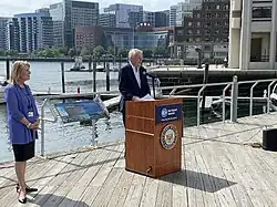 A man speaking at a podium as a woman looks on