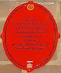 Oval red plaque bearing the words "In memory of District Officer Charles Pearson of the London Fire Brigade who died from injuries received at 100 Sidney Street near this site during the siege of Sidney Street on the 3rd of January 1911."