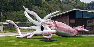 Statue of a giant pink and white squid in a grassy field