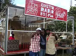 Glass building with red-and-white sign and three people in front