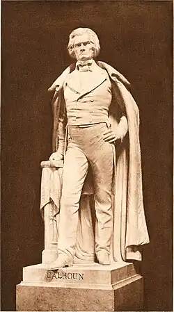 Life-sized statue, standing with full cloak to ankles, left hand on hip, right hand on book, serious and distinguished demeanor