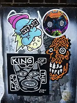 Stickers on a sign in Brick Lane, London by Rx Skulls, Dark Evil, ShallowLagoon and Nvrasir. 2025.