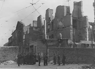 IPN copy #53 (No image caption, in section This is how the former Ghetto looks after having been destroyed) Nalewki Street, looking South at the gate at Nalewki/Gęsia/Franciszkańska intersection. Beyond the wall on the right Posner house at Nalewkach 29.