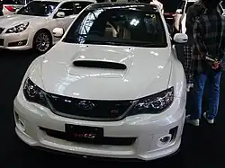 Subaru WRX STI tS, a lightened variant of the standard Subaru WRX STI sedan. This photo shows the front of the car, which is white; the car has been lightened by replacing the standard roof panel with carbon fiber, which is visible.