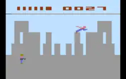 Pixel graphic image that represents a grey city skyline. A blue and red stick figure flies over the city.