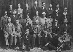 Black and white group photo of 27 men and women dressed in formal wear