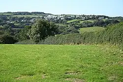 Treneglos: towards Warbstow Cross. On the skyline, left, is the hillfort Warbstow Bury. Largely hidden by trees, above the hedge, are buildings at Trewen; a farm which once had a mill barn powered by a waterwheel fed by a stream from the village