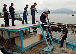 A number of men in blue uniforms with guns on the roof and deck of a wooden boat