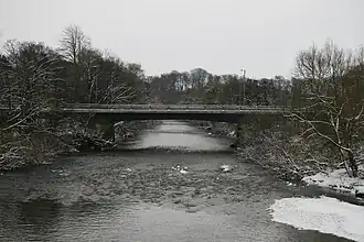 A wintry scene of a river, with a road bridge in the background