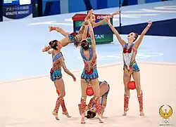 Three gymnasts lift a fourth
