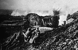 Photo of a German assault on Fort Vaux. In the foreground four German soldiers man two machine guns, while the fort can be seen in the background.