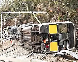 An image of the crash site with a Tangara train (set G7) lying on its side and bushland surrounding the railway.
