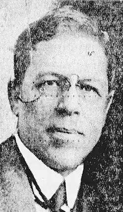 Black and white photo of a middle-aged man wearing eyeglasses, and a white high-collar dress shirt