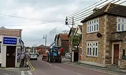 Street scene with houses and shops on both side of road on which there is a tractor.