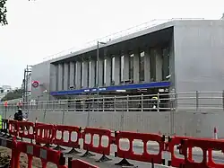 A grey-panelled building with a rectangular, dark blue sign reading "WOOD LANE STATION" in white letters all under a cloudy sky