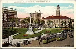 Postcard view of an urban common and city hall, with two streetcars on an adjacent street