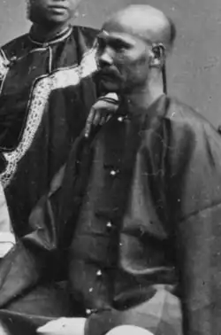 A greyscale image of Zeng Laisun, wearing a queue haircut and an official's coat. A young woman stands by him and rests her hand on his shoulder.